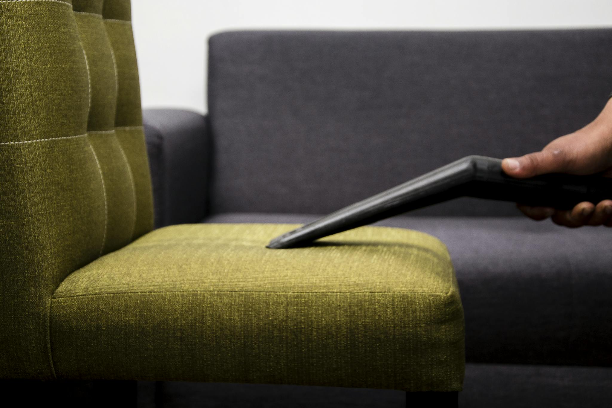 Close-up of a person vacuuming a modern sofa chair indoors, highlighting cleaning service.